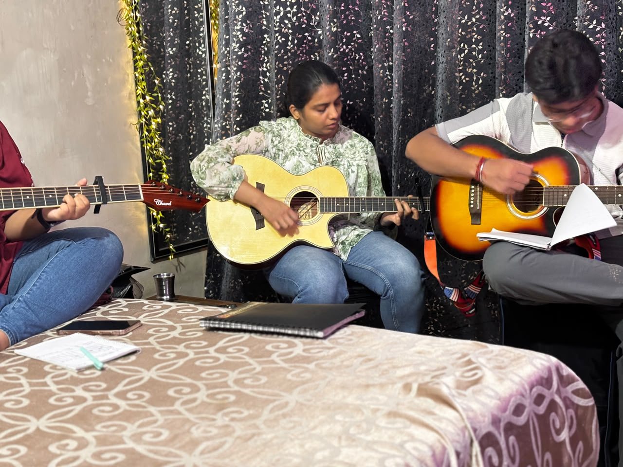 Three students playing acoustic guitars together during a jam session