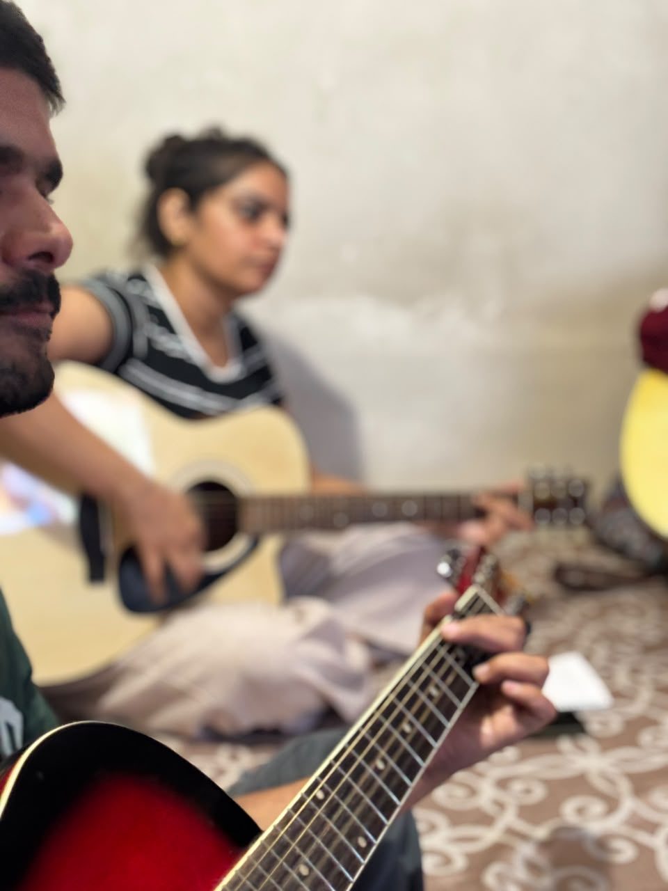 Students playing guitar together, seated on the floor during class